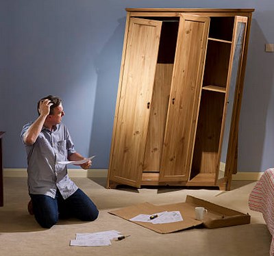 A man kneeling on the floor holding his head in front of a tall wooden cabinet that doesn't fit together
